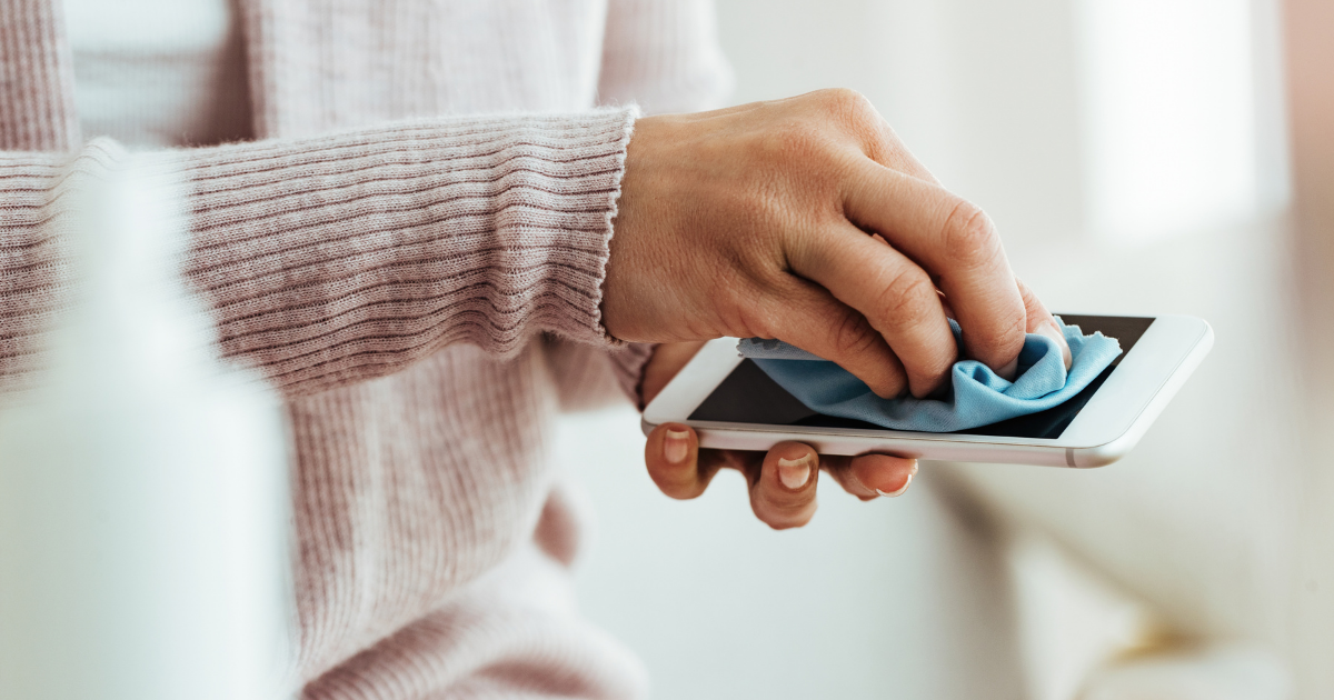 Nahaufnahme einer Person, die mit einem blauen Mikrofasertuch den Bildschirm eines Smartphones reinigt.