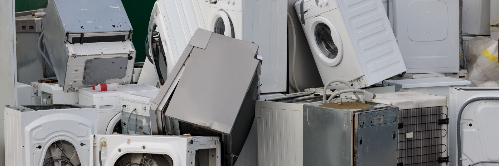 Haufen ausgedienter Haushaltsgeräte wie Waschmaschinen, Trockner und Geschirrspüler auf einem Recycling- oder Entsorgungsplatz.
