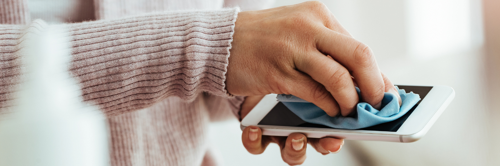 Nahaufnahme einer Person, die mit einem blauen Mikrofasertuch den Bildschirm eines Smartphones reinigt.