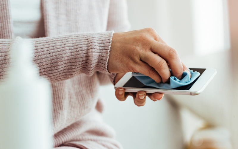 Nahaufnahme einer Person, die mit einem blauen Mikrofasertuch den Bildschirm eines Smartphones reinigt.