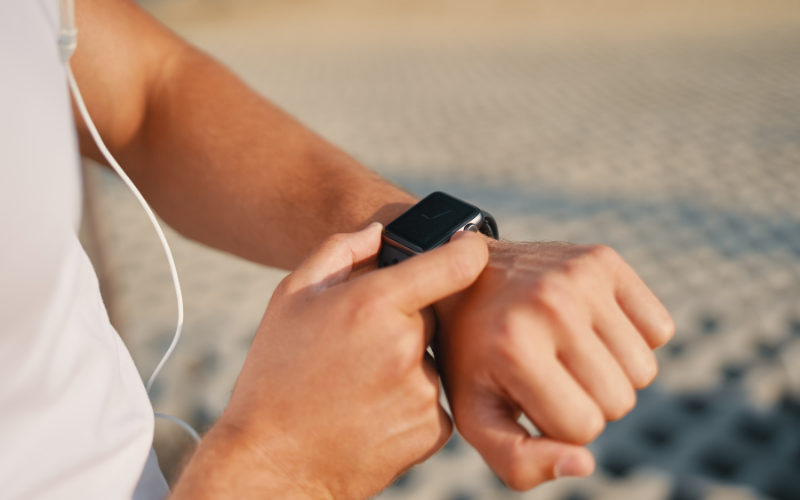 Nahaufnahme einer Person im Sportoutfit, die eine Smartwatch am Handgelenk bedient.