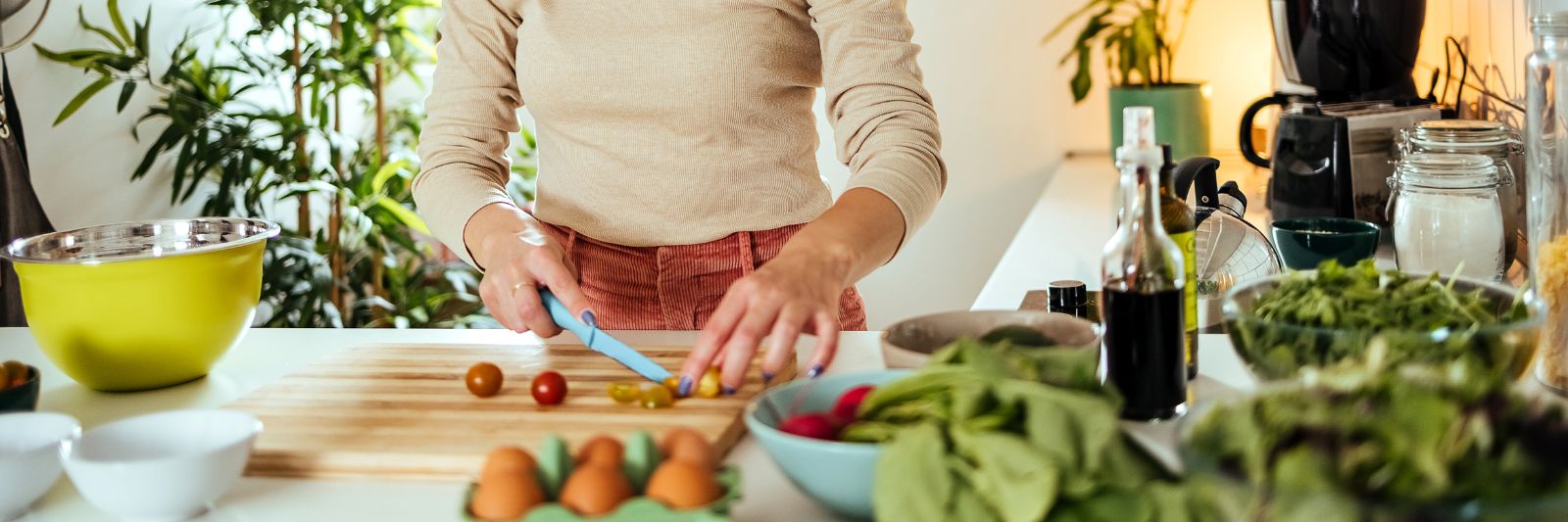 Frau schneidet in Küche Gemüse, dahinter Pflanze