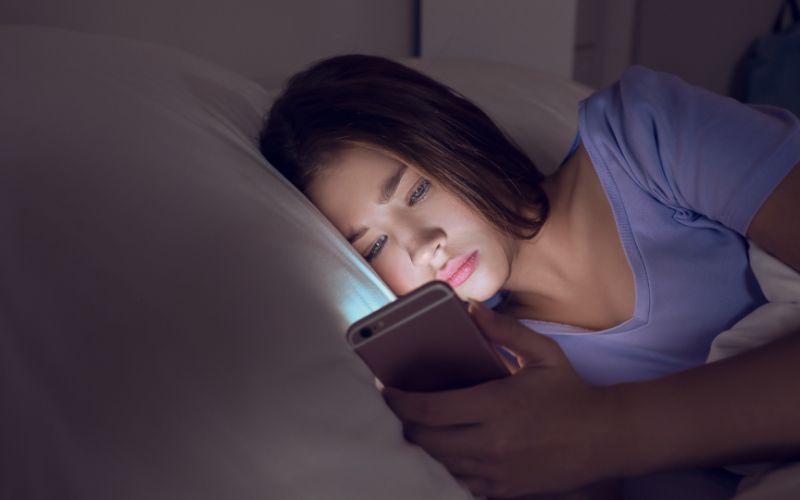 Junge Frau liegt im Bett und schaut auf ein Smartphone