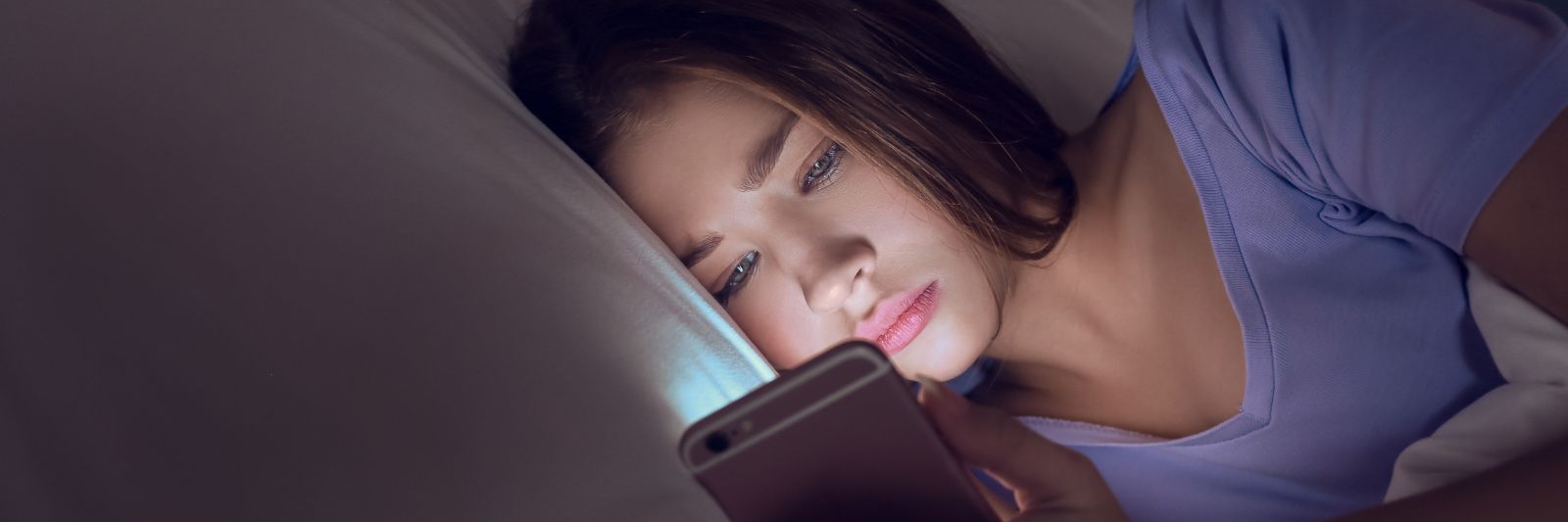 Junge Frau liegt im Bett und schaut auf ein Smartphone