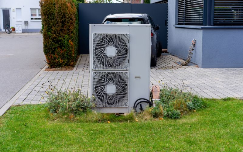 Wärmepumpe vor Haus auf Wiese, dahinter Auto