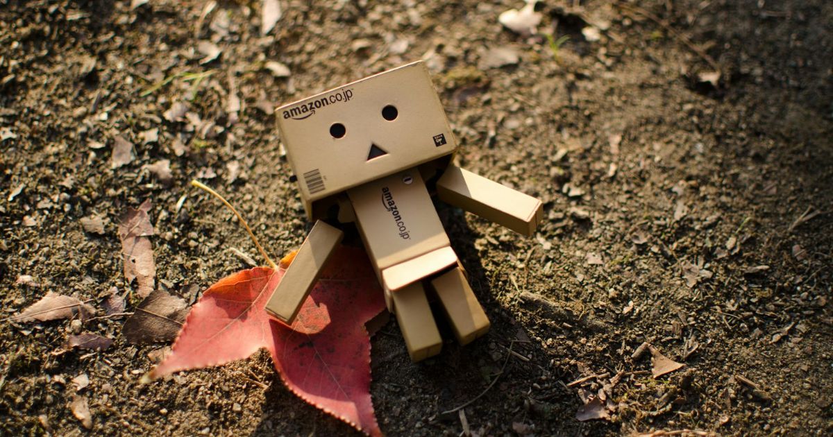 Mini-Roboter aus Pappe liegt auf Erde, daneben ein Blatt