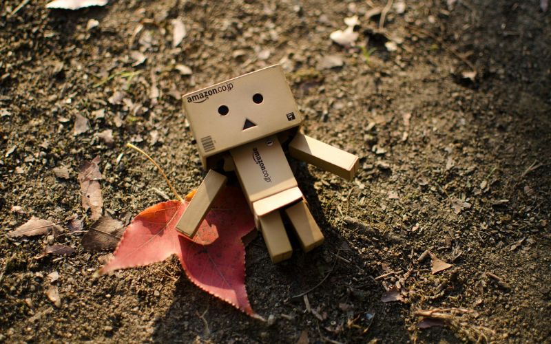 Mini-Roboter aus Pappe liegt auf Erde, daneben ein Blatt