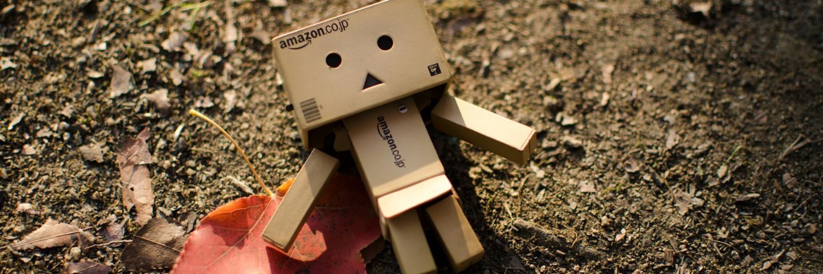Mini-Roboter aus Pappe liegt auf Erde, daneben ein Blatt