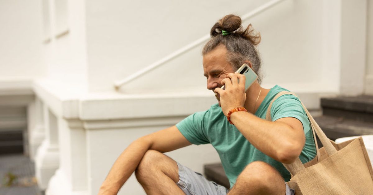 Mann sitzt und telefoniert, hat eine beige Tasche um die Schulter