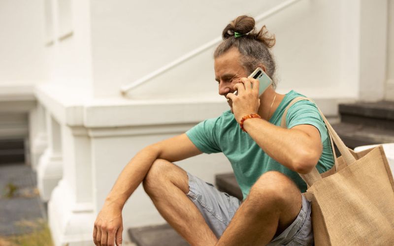 Mann sitzt und telefoniert, hat eine beige Tasche um die Schulter