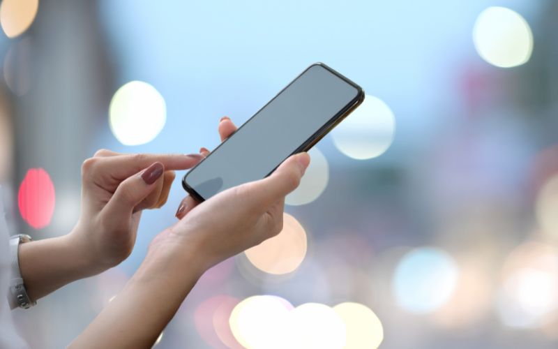 Handy wird in Hand gehalten, dahinter verschwommene Lichter