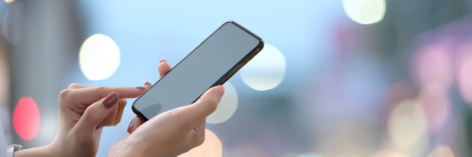 Handy wird in Hand gehalten, dahinter verschwommene Lichter