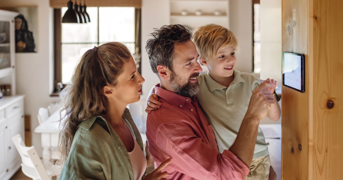 Vater, Mutter und Kind in Haus schauen auf Thermostat-Regler