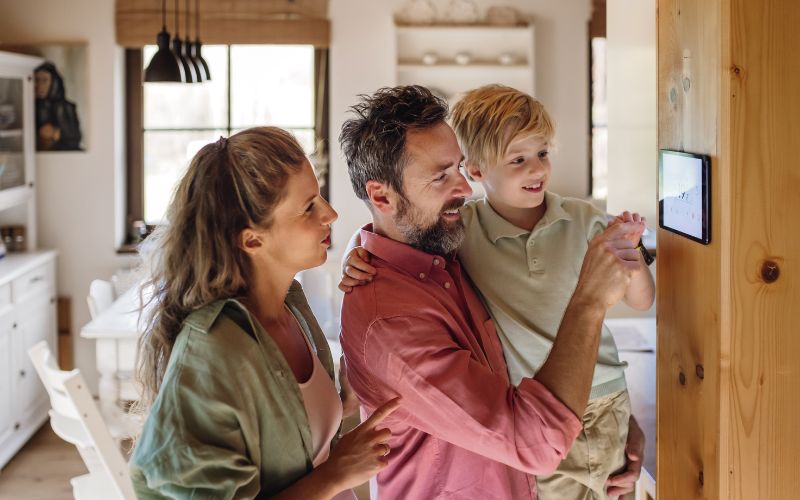 Vater, Mutter und Kind in Haus schauen auf Thermostat-Regler