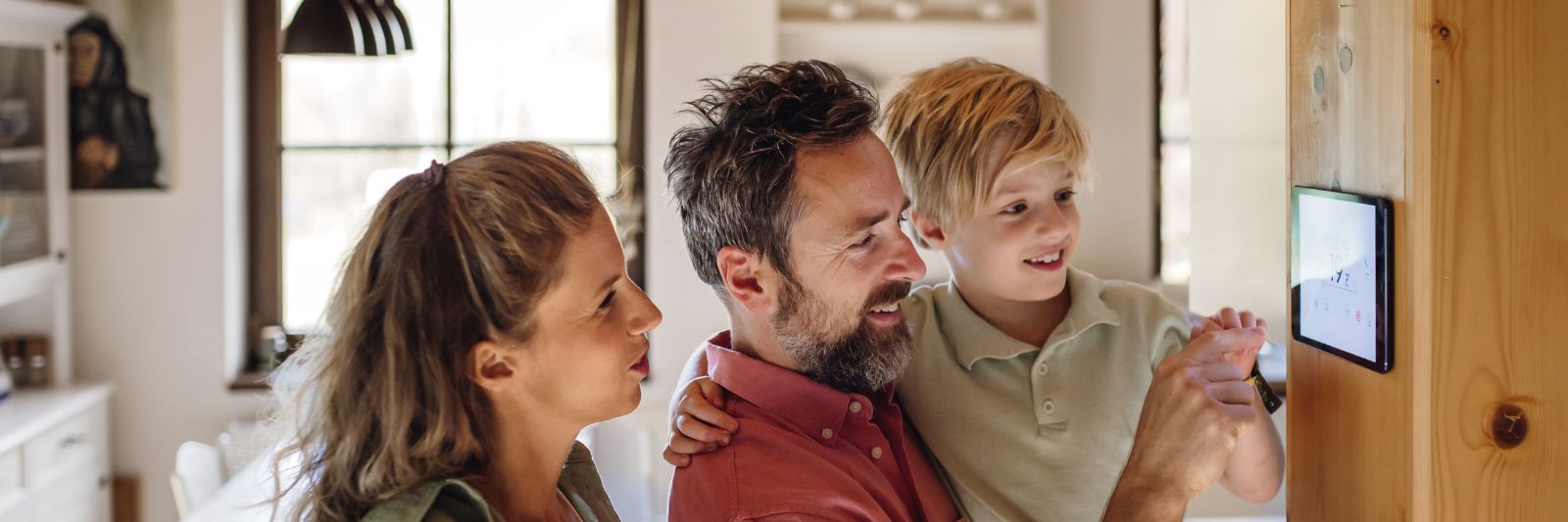 Vater, Mutter und Kind in Haus schauen auf Thermostat-Regler
