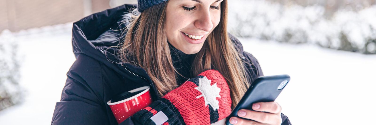 Eine Frau schaut auf ihr Handy, hinter ihr ein verschneiter Garten mit Mauer