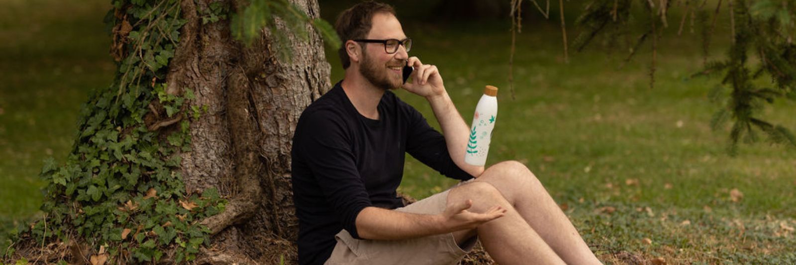 Mann sitzt am Baum im Park und telefoniert