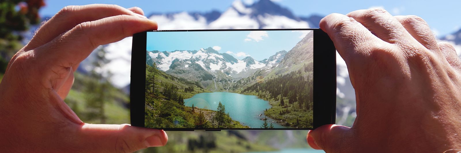 Mensch macht Foto mit Smartphone, im Hintergrund Berge, Wälder und See