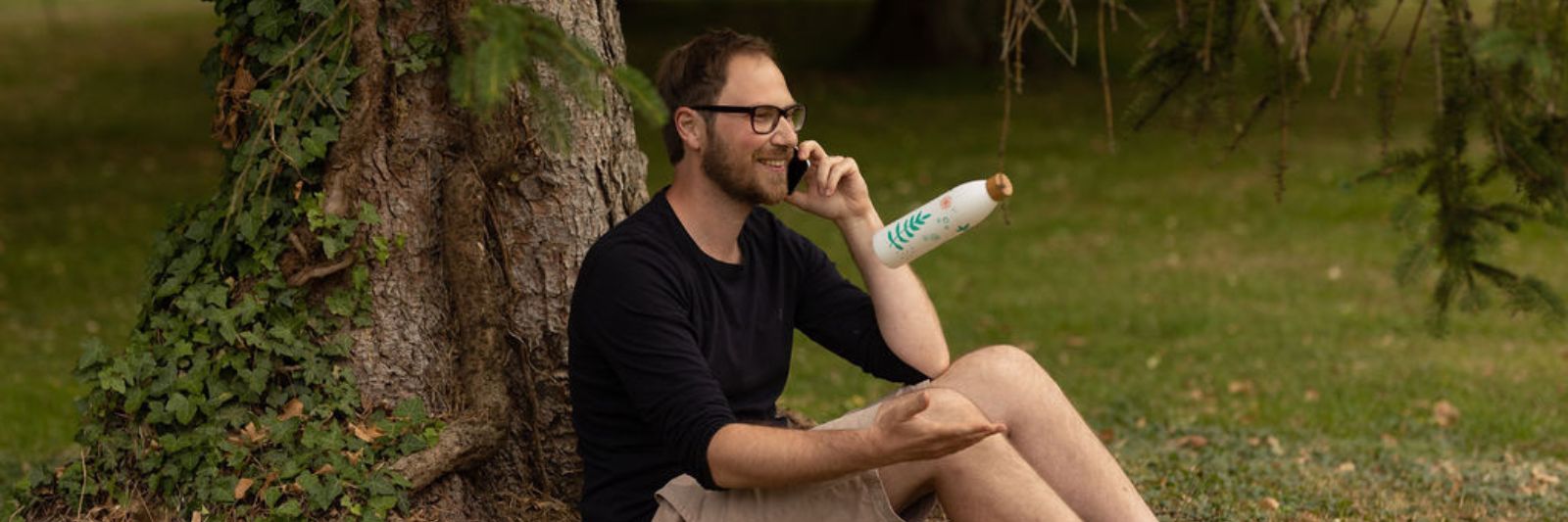 Mann sitzt telefonierend an einem Baum