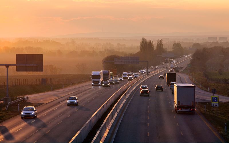 Autos und LKWs fahren auf einer Autobahn, daneben Bäume