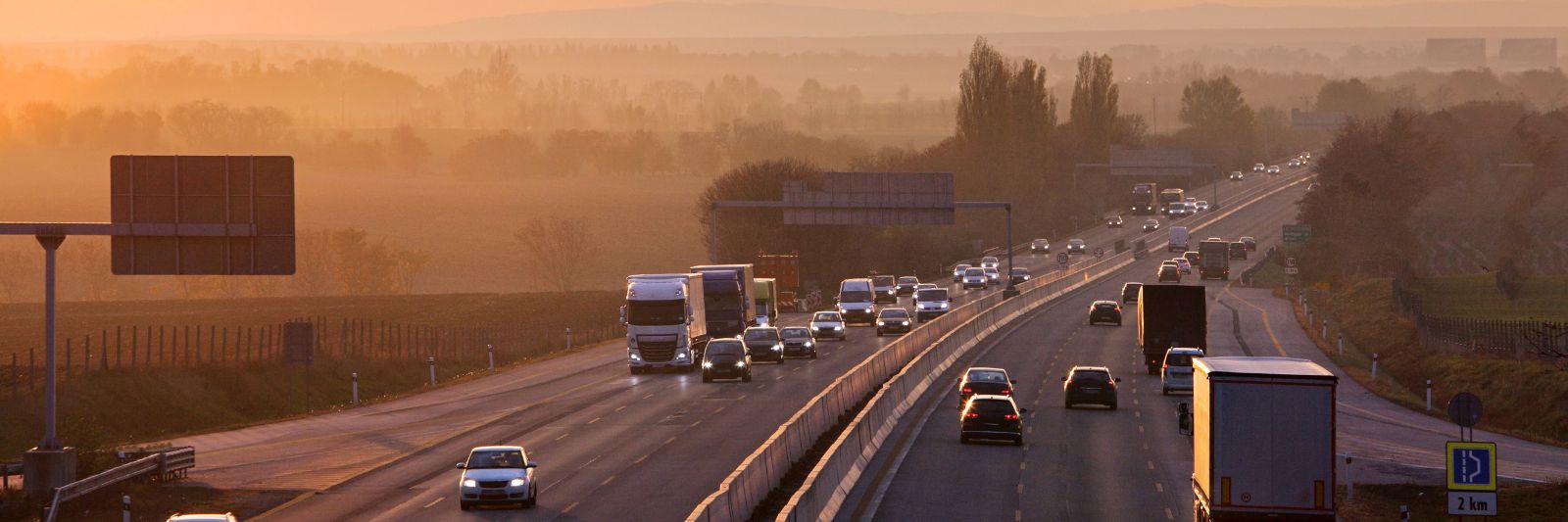 Autos und LKWs fahren auf einer Autobahn, daneben Bäume