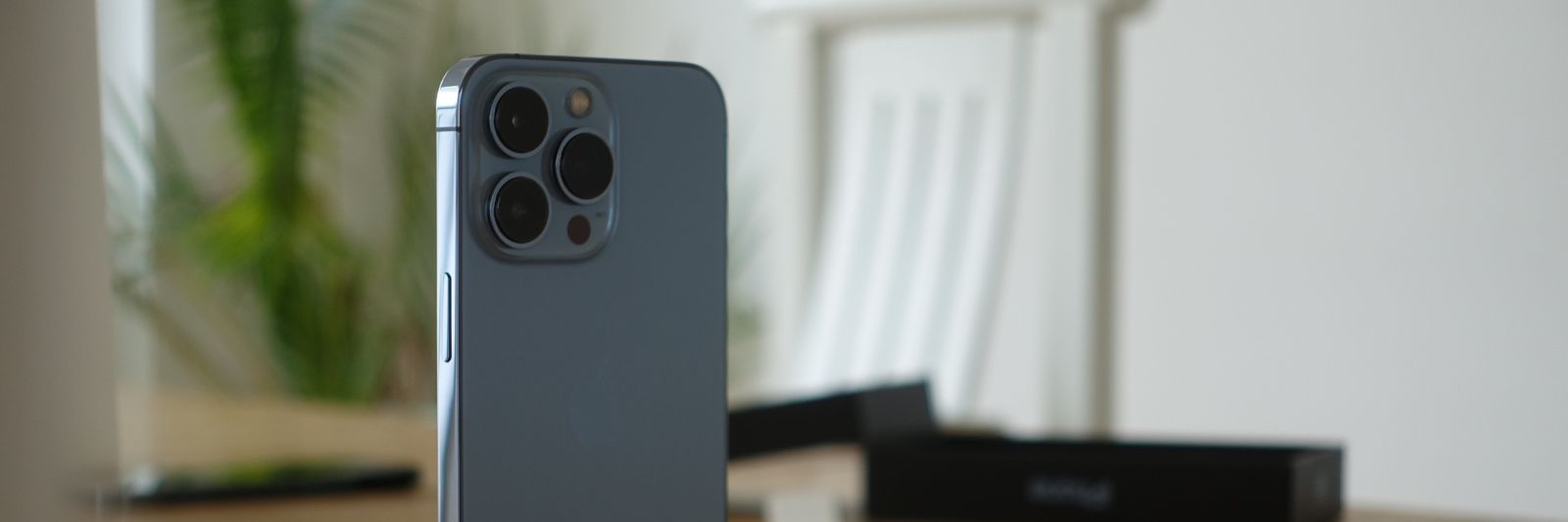 iPhone steht auf Tisch, dahinter Stuhl und Pflanze